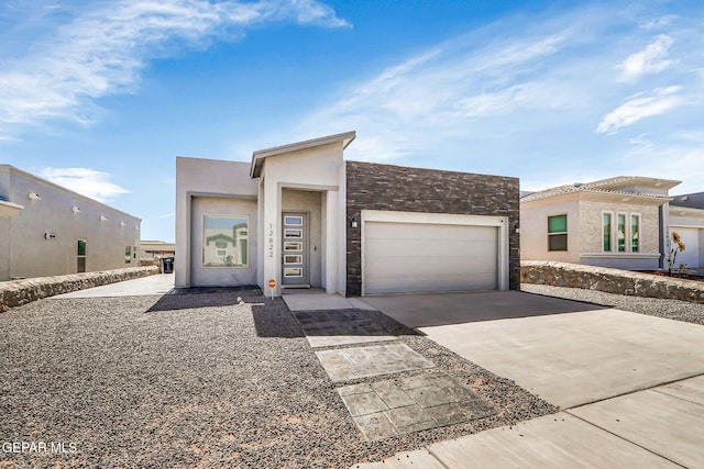 contemporary home with a garage, driveway, stone siding, and stucco siding