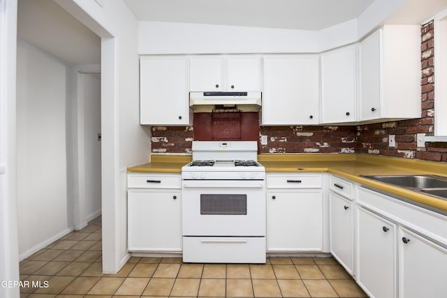 kitchen with white gas stove, light countertops, white cabinets, light tile patterned flooring, and under cabinet range hood