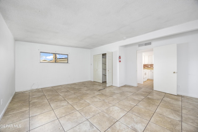 spare room with light tile patterned floors, baseboards, visible vents, and a textured ceiling