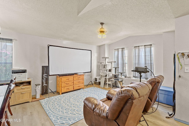 home theater with lofted ceiling, light wood-style floors, a textured ceiling, and a ceiling fan