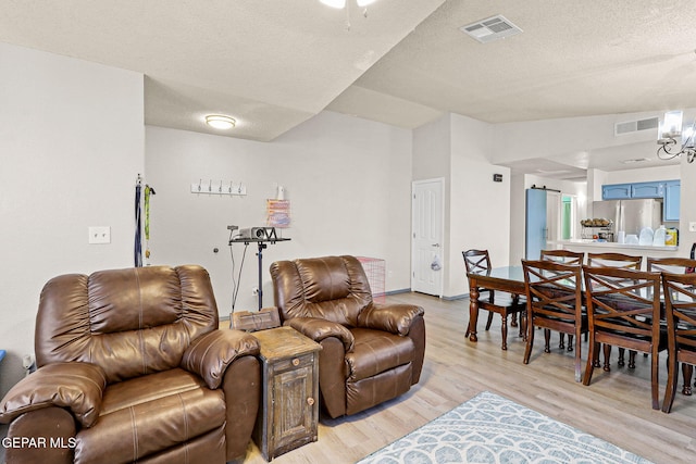 living area with visible vents, a textured ceiling, light wood finished floors, and a barn door