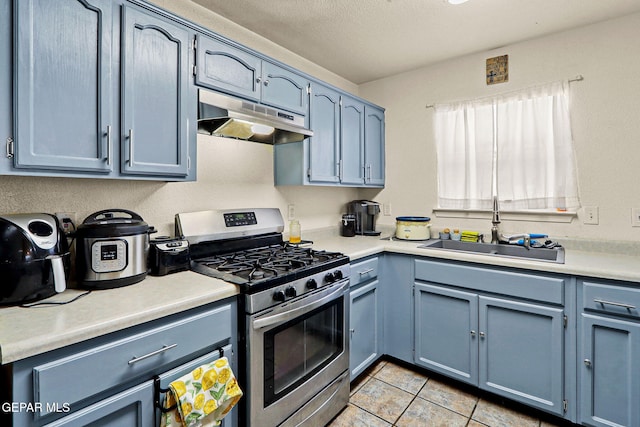 kitchen with blue cabinets, stainless steel gas stove, a sink, and under cabinet range hood