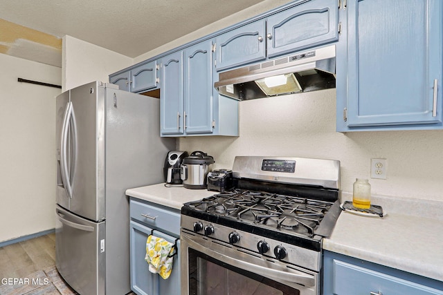 kitchen with stainless steel appliances, blue cabinetry, light countertops, and under cabinet range hood