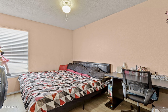 bedroom with a textured ceiling, baseboards, and wood finished floors