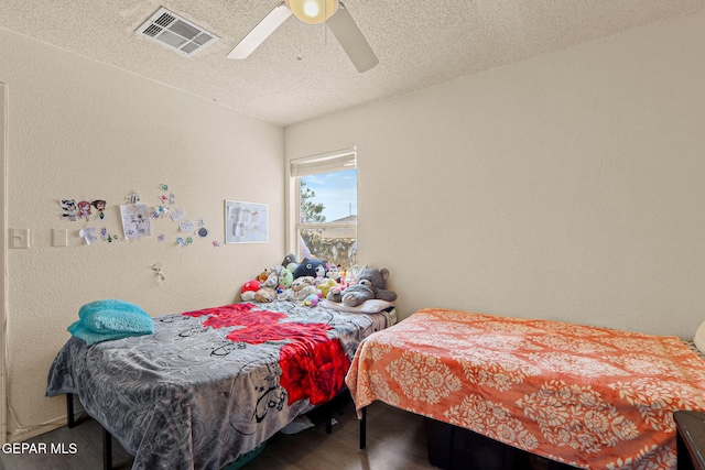 bedroom with visible vents, a textured wall, ceiling fan, wood finished floors, and a textured ceiling