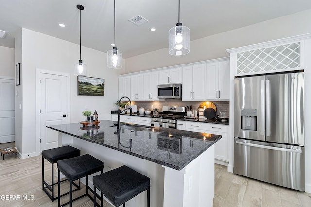 kitchen with a center island with sink, visible vents, appliances with stainless steel finishes, white cabinetry, and backsplash