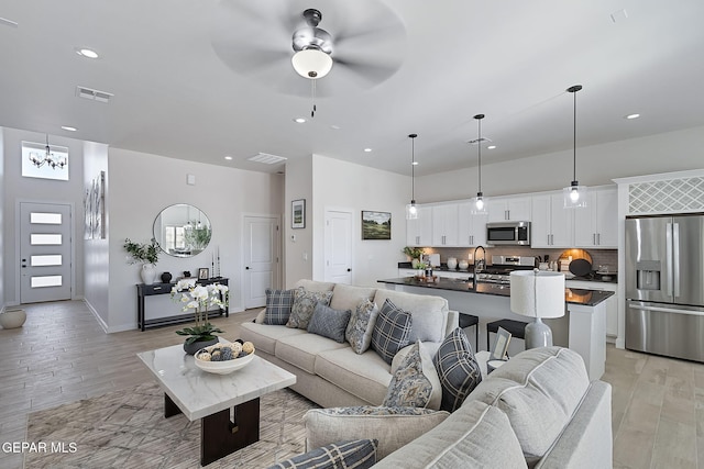 living room featuring light wood finished floors, recessed lighting, visible vents, baseboards, and ceiling fan with notable chandelier