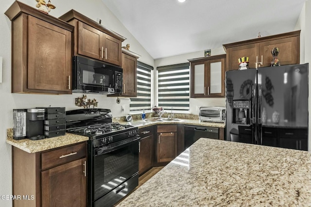 kitchen with light stone countertops, a toaster, lofted ceiling, black appliances, and a sink