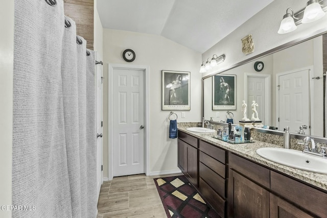 full bathroom with vaulted ceiling, double vanity, baseboards, and a sink