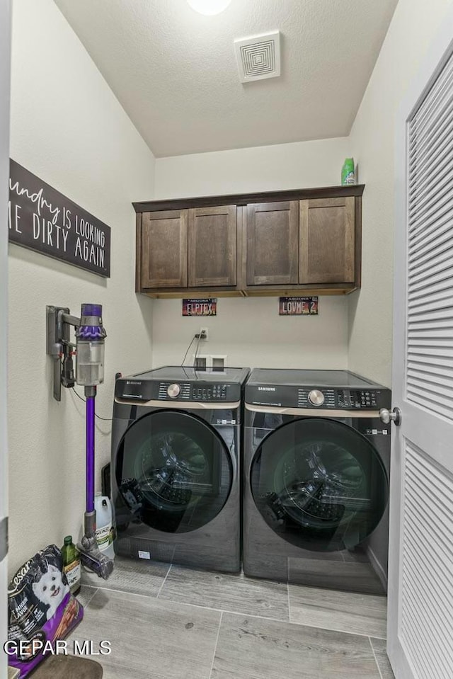 laundry room with visible vents, wood tiled floor, cabinet space, a textured ceiling, and washing machine and dryer