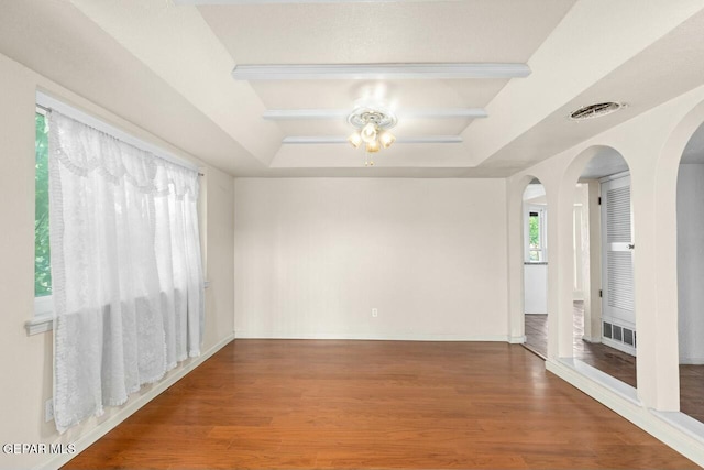 spare room with arched walkways, a raised ceiling, visible vents, wood finished floors, and baseboards