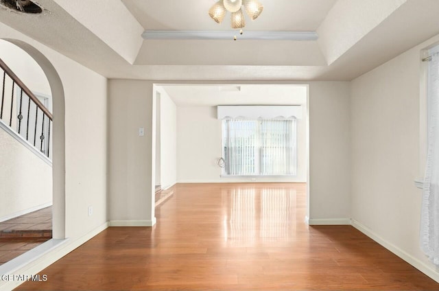 interior space with arched walkways, a raised ceiling, and wood finished floors