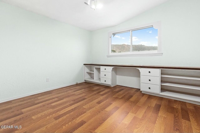 unfurnished office with light wood-type flooring, built in desk, and baseboards