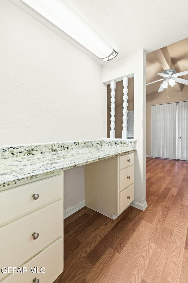 kitchen featuring baseboards, dark wood-style floors, light stone countertops, white cabinetry, and built in desk