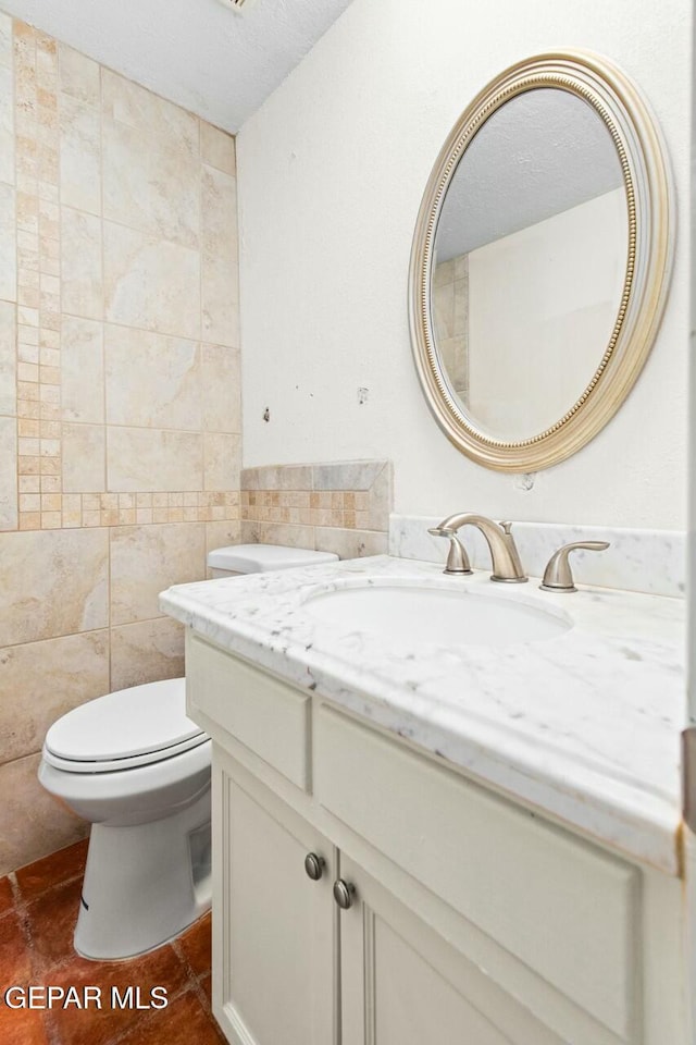 half bath with toilet, tile patterned flooring, tile walls, and vanity