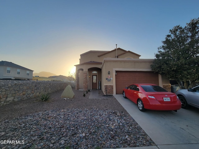 view of front facade featuring an attached garage, stone siding, concrete driveway, and stucco siding