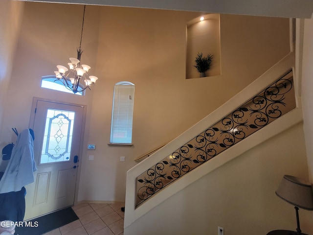 foyer entrance with a high ceiling, light tile patterned floors, an inviting chandelier, and stairs