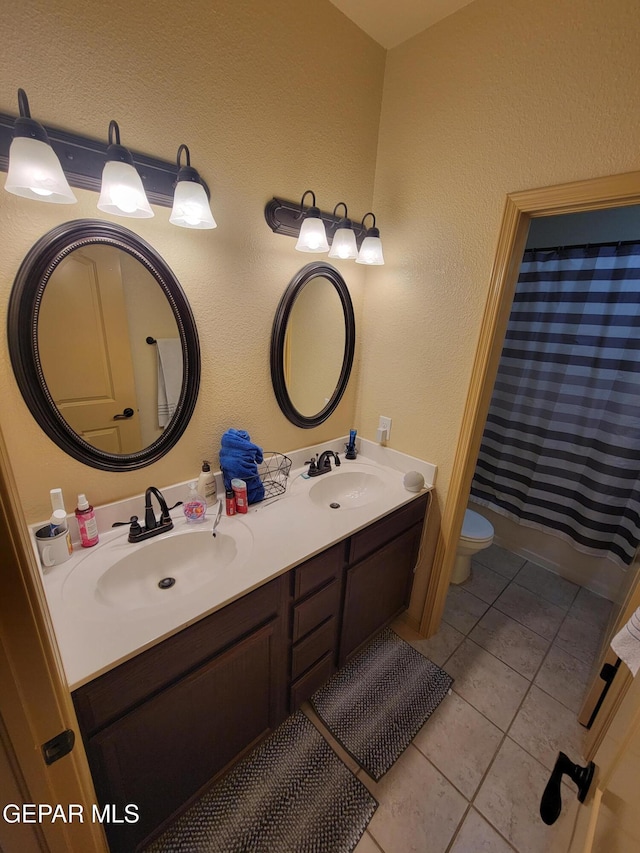 bathroom with tile patterned floors, a sink, toilet, and double vanity