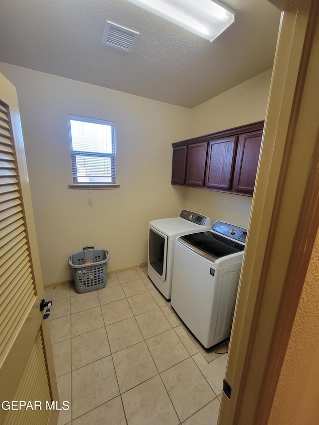 laundry room featuring washing machine and clothes dryer, visible vents, cabinet space, light tile patterned flooring, and a textured ceiling