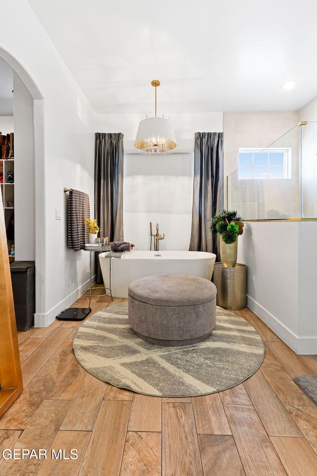 full bath featuring a soaking tub, wood finished floors, baseboards, and a tile shower