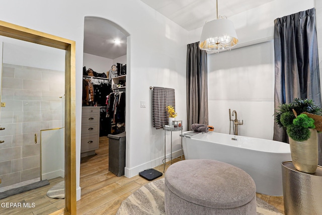 bathroom featuring wood finished floors, baseboards, a freestanding bath, a shower stall, and a spacious closet