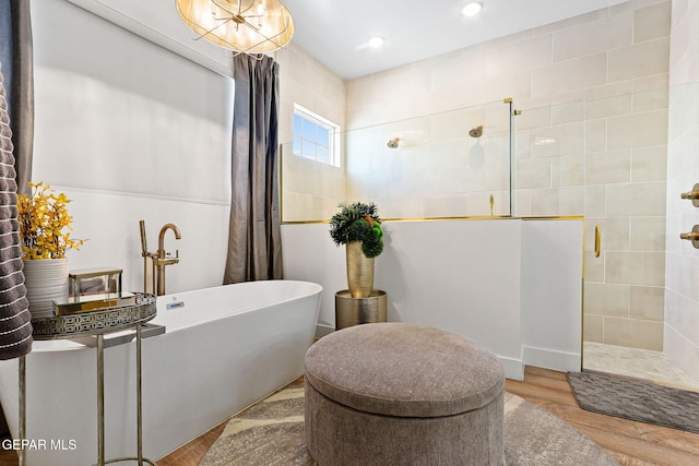 bathroom featuring a soaking tub, wood finished floors, and a tile shower