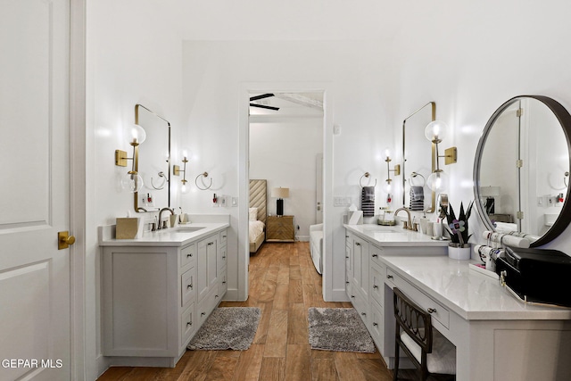 full bath featuring a sink, wood finished floors, two vanities, and ensuite bath