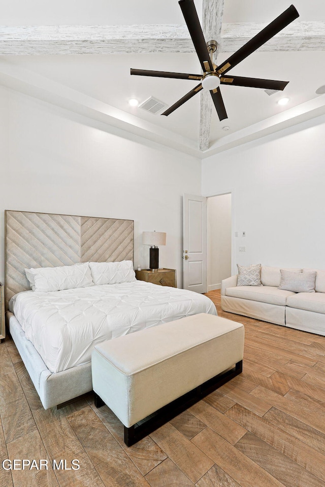 bedroom featuring a ceiling fan, a tray ceiling, wood finished floors, and visible vents