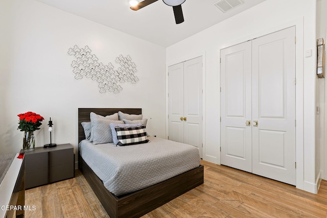 bedroom featuring light wood finished floors, visible vents, two closets, and ceiling fan