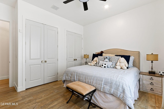 bedroom with a ceiling fan, visible vents, baseboards, light wood-style flooring, and two closets