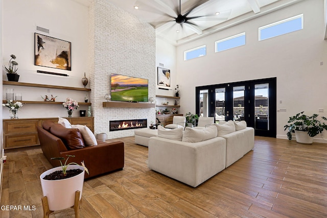 living area with baseboards, a fireplace, hardwood / wood-style flooring, a towering ceiling, and beamed ceiling