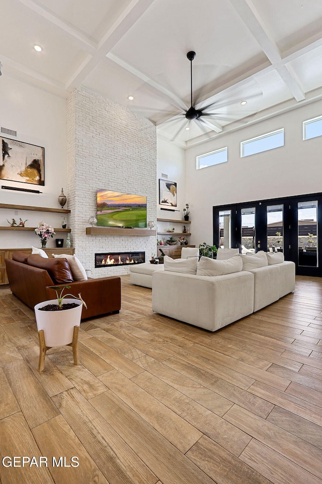 living room with wood finished floors, visible vents, coffered ceiling, a high ceiling, and a fireplace