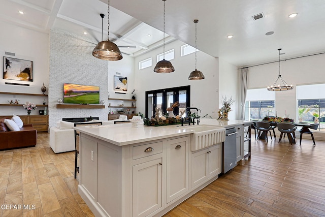 kitchen featuring light wood-type flooring, a kitchen island with sink, a sink, coffered ceiling, and open floor plan