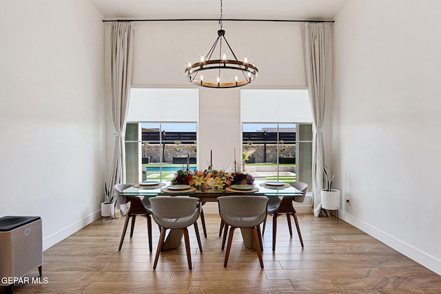 dining room featuring baseboards, wood finished floors, a chandelier, and a towering ceiling