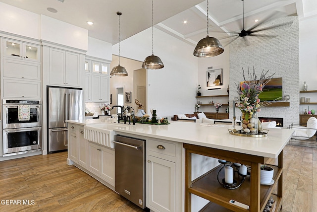 kitchen with light wood finished floors, open floor plan, light countertops, appliances with stainless steel finishes, and a kitchen island with sink