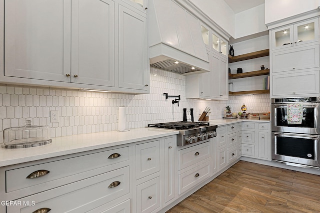 kitchen with light countertops, custom range hood, dark wood-style flooring, stainless steel appliances, and open shelves