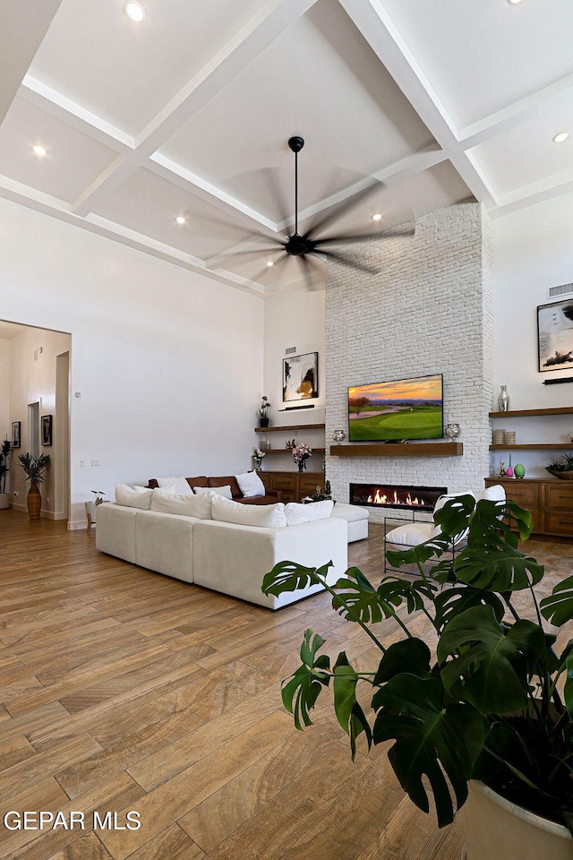 living area with wood finished floors, a ceiling fan, coffered ceiling, a fireplace, and beamed ceiling