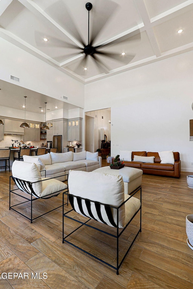 living area with visible vents, coffered ceiling, wood finished floors, and a towering ceiling