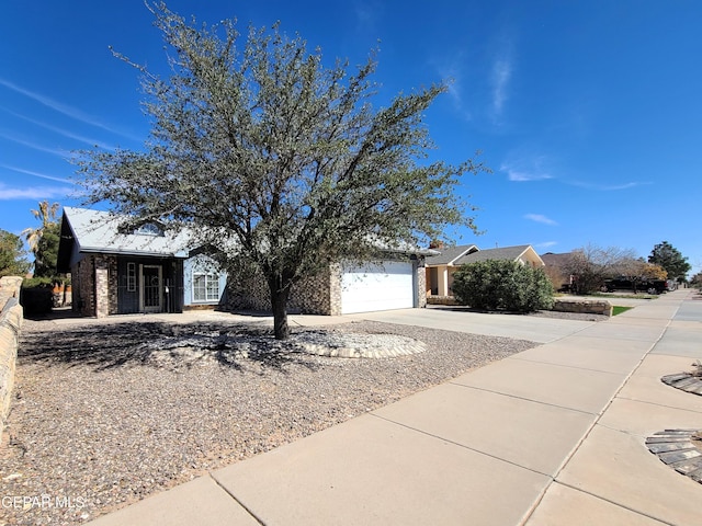 view of property hidden behind natural elements featuring a garage and concrete driveway