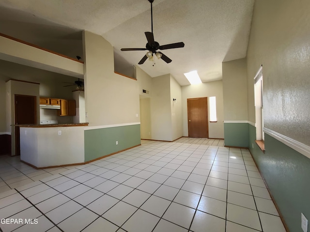 empty room with a textured ceiling, a skylight, light tile patterned floors, baseboards, and ceiling fan