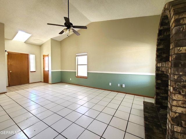 tiled empty room with baseboards, lofted ceiling with skylight, a textured ceiling, and a ceiling fan