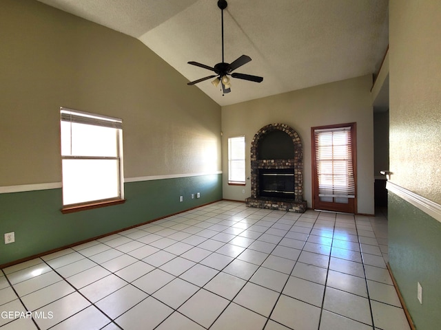 unfurnished living room with a brick fireplace, light tile patterned flooring, a ceiling fan, and baseboards