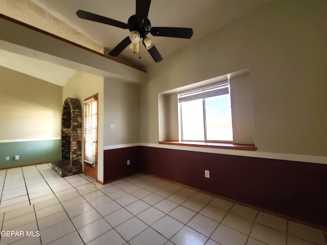 empty room featuring light tile patterned floors, a fireplace with raised hearth, and ceiling fan