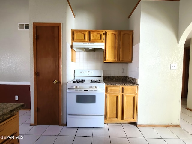 kitchen featuring visible vents, white range with gas cooktop, under cabinet range hood, light tile patterned floors, and decorative backsplash