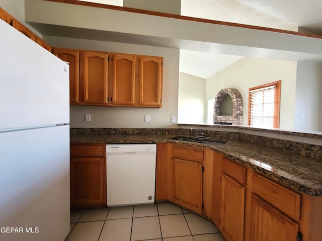 kitchen featuring a sink, white appliances, light tile patterned flooring, brown cabinetry, and vaulted ceiling