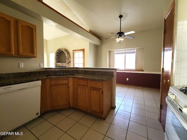 kitchen with a sink, dark countertops, white appliances, a peninsula, and light tile patterned floors