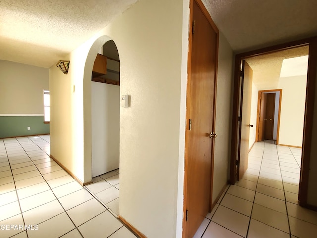 hallway featuring light tile patterned flooring, arched walkways, and a textured ceiling