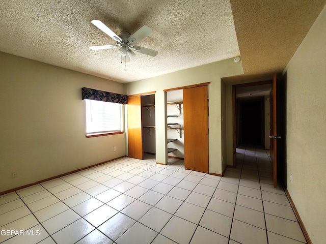 unfurnished bedroom with light tile patterned flooring, a ceiling fan, baseboards, and two closets