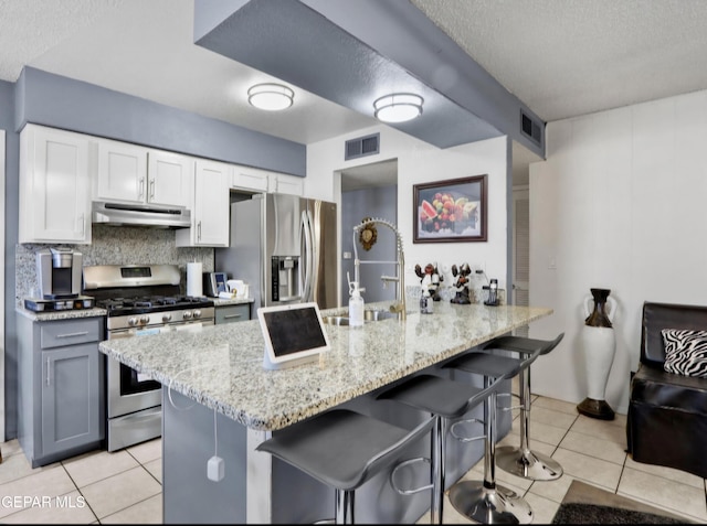 kitchen with visible vents, appliances with stainless steel finishes, a breakfast bar area, light stone countertops, and under cabinet range hood