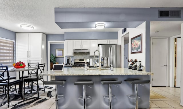 kitchen with light tile patterned floors, stainless steel appliances, visible vents, a sink, and under cabinet range hood